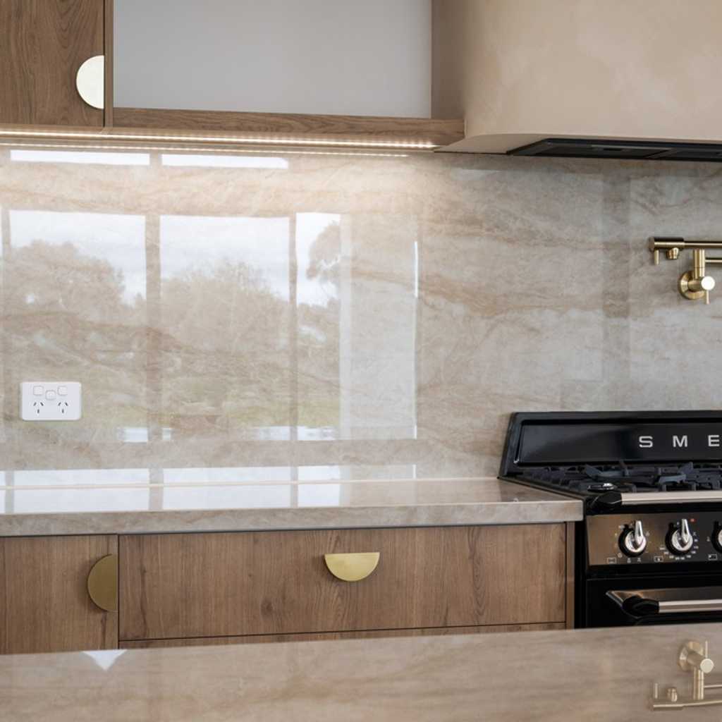 Freestanding Smeg Cooker with brushed brass pot filler amongst a sea of polished stone benchtops that seamlessly flow up the backsplash.