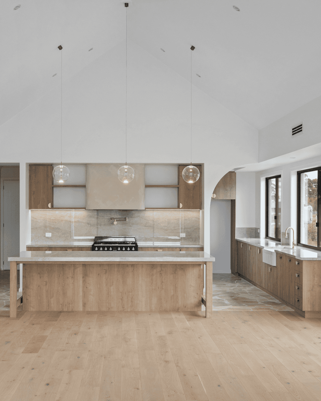Luxury coastal farmhouse kitchen with cathedral style ceilings and a half arch entryway into the butlers pantry.